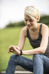 Smiling young woman checking her smartwatch - TAMF00826