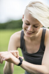 Smiling young woman checking her smartwatch - TAMF00827