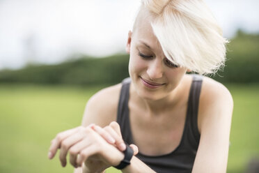 Smiling young woman checking her smartwatch - TAMF00828