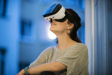 Junge Frau sitzt am Fenster und trägt eine Virtual-Reality-Brille - TAMF00845