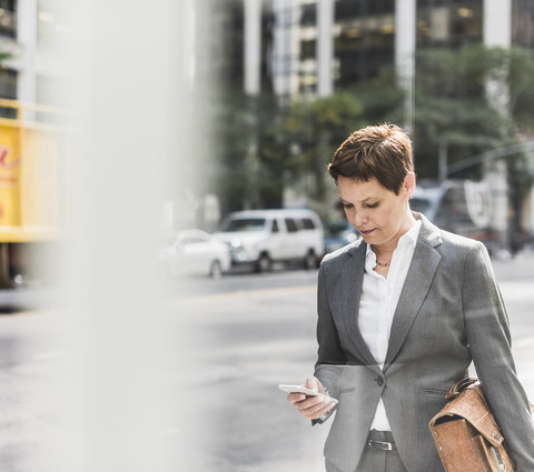 USA, New York City, Geschäftsfrau in Manhattan schaut auf ein Handy, lizenzfreies Stockfoto