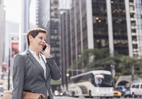 USA, New York City, Geschäftsfrau in Manhattan, die mit einem Handy telefoniert - UUF09391