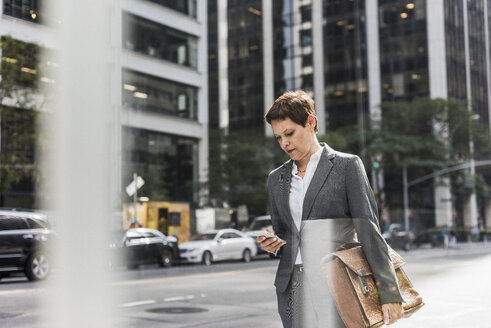 USA, New York City, Geschäftsfrau in Manhattan schaut auf ein Handy - UUF09393