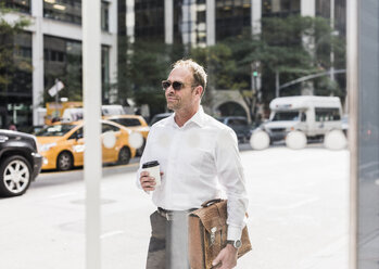 USA, New York City, selbstbewusster Geschäftsmann in Manhattan mit Kaffee zum Mitnehmen - UUF09396