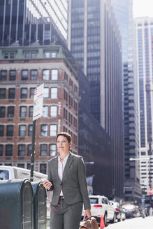 USA, New York City, Geschäftsfrau in Manhattan mit Mobiltelefon und Kopfhörern - UUF09402