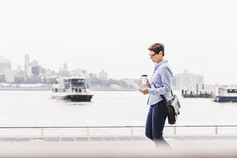 USA, New York City, Geschäftsfrau, die am East River spazieren geht und ein Dokument liest, lizenzfreies Stockfoto
