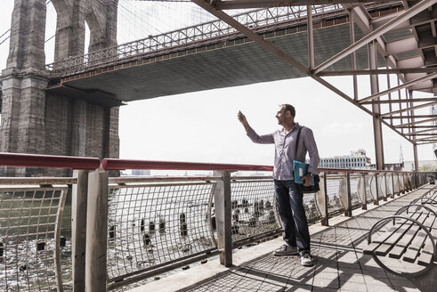 USA, New York City, Mann am East River mit Mobiltelefon in der Hand - UUF09422