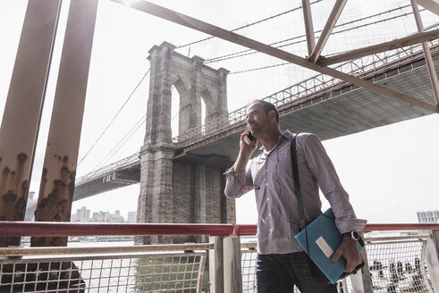 USA, New York City, Mann am East River, der mit einem Handy telefoniert - UUF09423