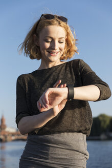 Lächelnde junge Frau überprüft ihre Smartwatch - TAMF00859