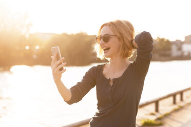 Happy young woman taking selfie with smartphone at backlight - TAMF00862