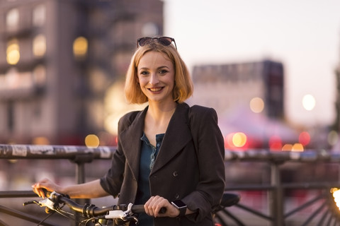 Portrait of smiling young woman with bicycle at evening twilight stock photo