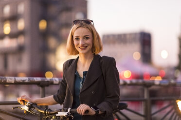 Porträt einer lächelnden jungen Frau mit Fahrrad in der Abenddämmerung - TAMF00880