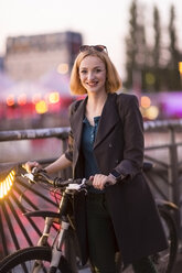 Porträt einer glücklichen jungen Frau mit Fahrrad in der Abenddämmerung - TAMF00881