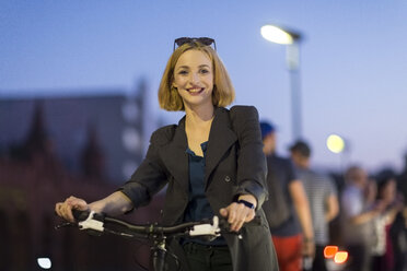 Deutschland, Berlin, Porträt einer lächelnden jungen Frau mit Fahrrad in den Abendstunden - TAMF00884