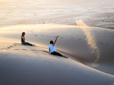 Oman, Al Raka, zwei junge Frauen sitzen auf einer Düne in der Wüste Rimal Al Wahiba, lizenzfreies Stockfoto