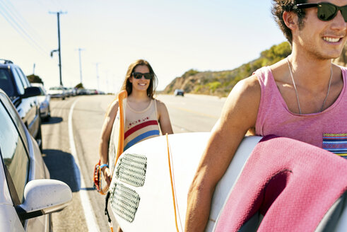 Lächelndes junges Paar mit Surfbrettern an der Küstenstraße - WESTF21988