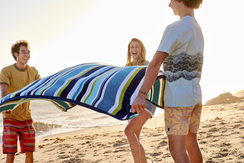 Glückliche Freunde breiten ihr Handtuch am Strand aus - WESTF22052