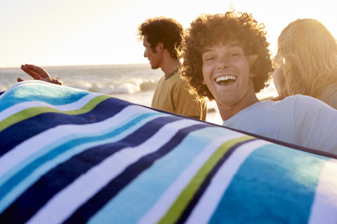 Glücklicher junger Mann mit Handtuch am Strand, lizenzfreies Stockfoto