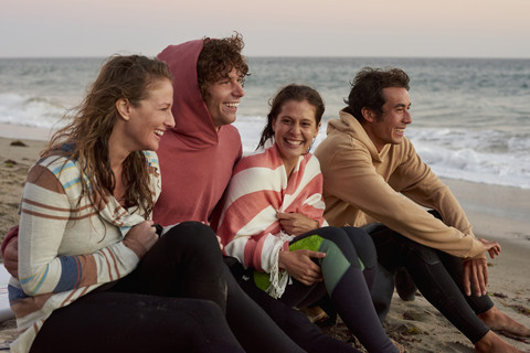 Happy friends sitting on the beach in the evening stock photo