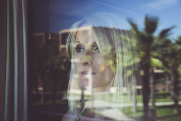 Woman looking out of window with reflecting palm trees - CHPF00354