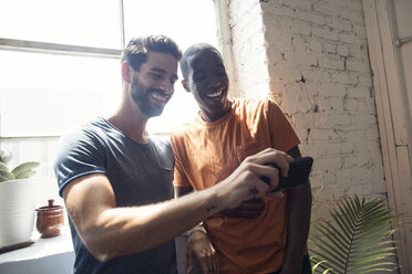 Zwei glückliche junge Männer mit Handy in einem Loft - WESTF22081