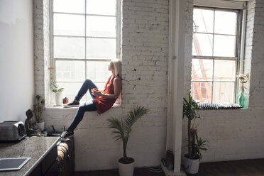 Young woman sitting on windowsill in a loft - WESTF22083