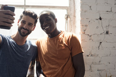 Zwei lächelnde junge Männer machen ein Selfie am Fenster - WESTF22084