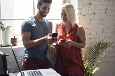 Smiling young man and woman with cell phones in a loft - WESTF22086