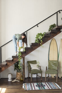 Junge Frau auf einer Treppe in einem Loft, die sich um eine Topfpflanze kümmert - WESTF22099