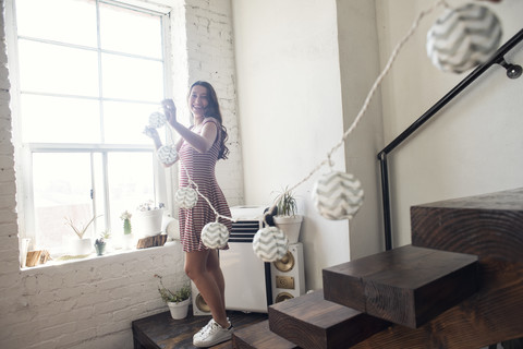 Junge Frau dekoriert Loft mit Fairylights, lizenzfreies Stockfoto