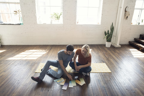 Junges Paar sitzt auf Teppich in einem Loft und betrachtet Farbmuster, lizenzfreies Stockfoto