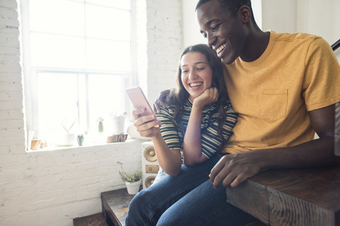 Happy young couple sitting on stairs in a loft sharing cell phone stock photo