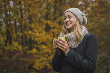 Smiling young woman with hot beverage in autumn forest - KKAF00079
