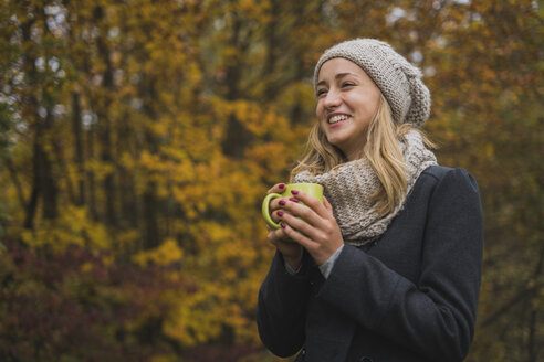 Lächelnde junge Frau mit heißem Getränk im Herbstwald - KKAF00079