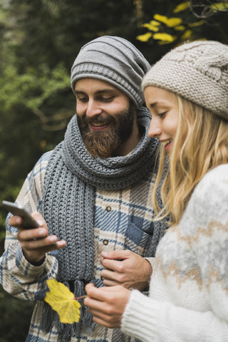 Junges Paar im Freien im Herbst schaut auf Handy, lizenzfreies Stockfoto