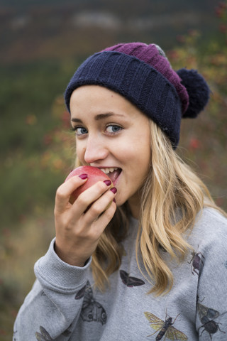 Porträt einer lächelnden jungen Frau, die einen Apfel im Freien isst, lizenzfreies Stockfoto