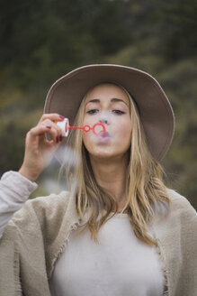 Junge Frau mit Hut beim Blasen von Seifenblasen - KKAF00100