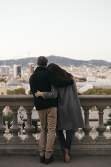 Spanien, Barcelona, Rückenansicht eines Paares Arm in Arm mit Blick auf die Stadt - KKAF00147