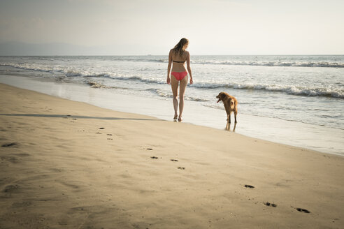 Mexiko, Riviera Nayarit, Frau geht mit Hund am Strand spazieren - ABAF02099