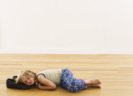 Little boy lying on wooden floor with head on slippers - FSF00634