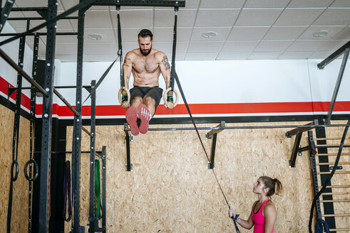 Mann macht Übungen an Ringen im Fitnessstudio mit Frau, die ihm hilft - KIJF00939