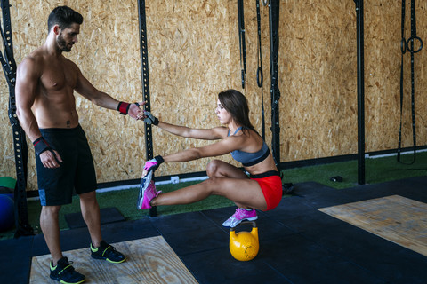 Mann hilft Frau beim Halten des Gleichgewichts auf einer Kettlebell im Fitnessstudio, lizenzfreies Stockfoto