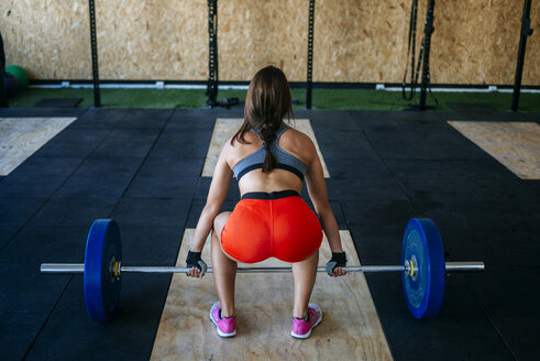 Rückenansicht einer Frau, die sich auf das Heben einer Langhantel im Fitnessstudio vorbereitet - KIJF00959