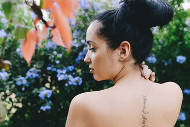 Woman with an arabic tattoo on her back surrounded by flowers and vegetation - GEMF01280