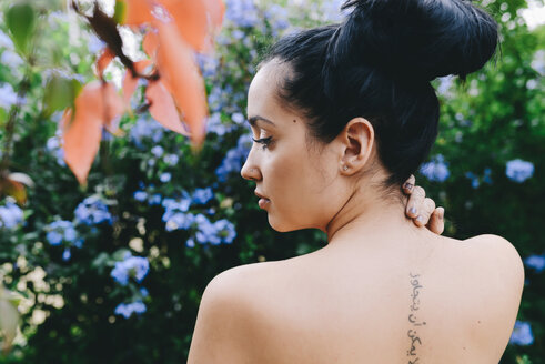 Frau mit einer arabischen Tätowierung auf dem Rücken, umgeben von Blumen und Vegetation - GEMF01280
