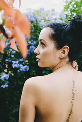 Woman with an arabic tattoo on her back surrounded by flowers and vegetation - GEMF01281