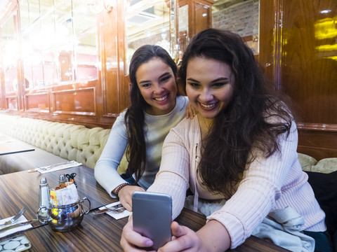 Zwei junge Frauen nehmen Selfie mit Handy in einem Restaurant, lizenzfreies Stockfoto