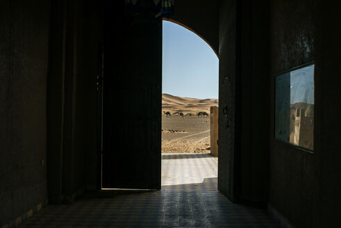 Marokko, Merzouga, Blick durch ein Tor auf eine Landschaft mit Kamelen in der Wüste Erg Chebbi - KIJF00999