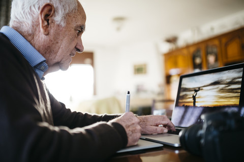 Senior-Fotograf bei der Arbeit mit Laptop, lizenzfreies Stockfoto