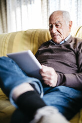 Älterer Mann sitzt auf der Couch und benutzt ein Tablet - JRFF01065